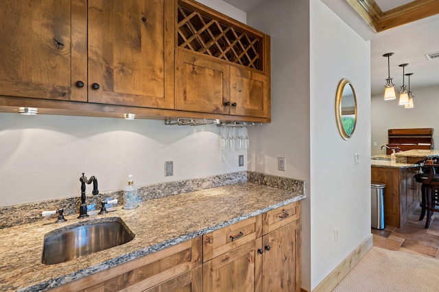 kitchen featuring a sink, light stone counters, baseboards, and brown cabinetry