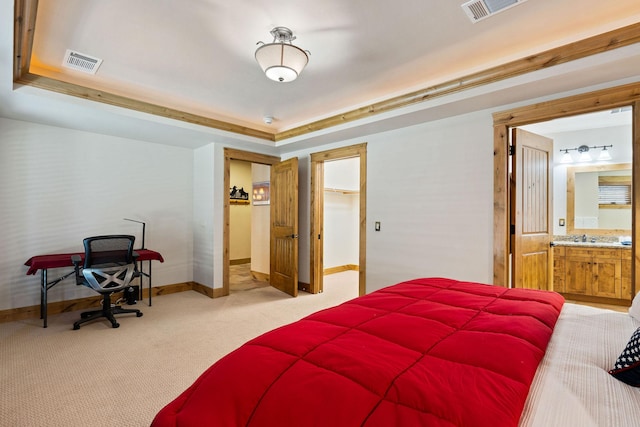 bedroom featuring baseboards, light colored carpet, a raised ceiling, a spacious closet, and connected bathroom