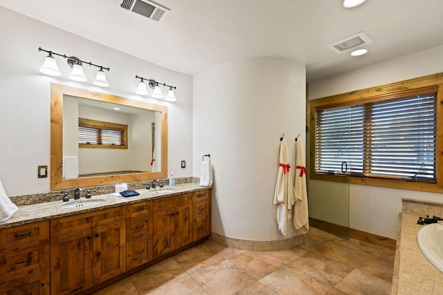 bathroom featuring tiled tub, double vanity, and baseboards