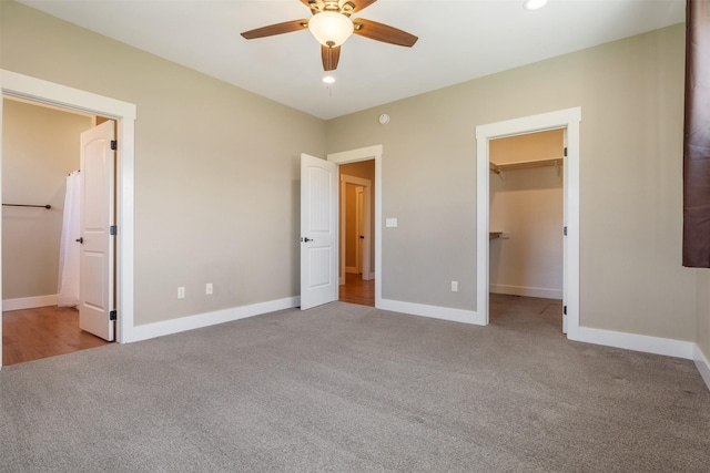 unfurnished bedroom featuring carpet floors, a walk in closet, baseboards, ceiling fan, and ensuite bath