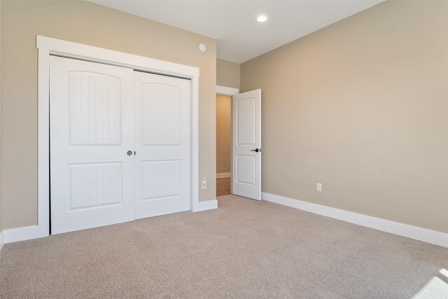unfurnished bedroom featuring light carpet, a closet, baseboards, and recessed lighting