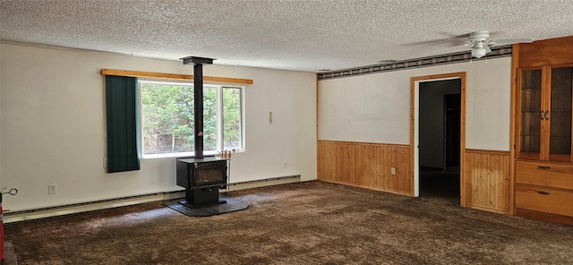 11169 Stemple Pass Rd, Lincoln, MT 59639 - carpeted spare room with a wood stove, wood walls, a baseboard heating unit, wainscoting, and ceiling fan