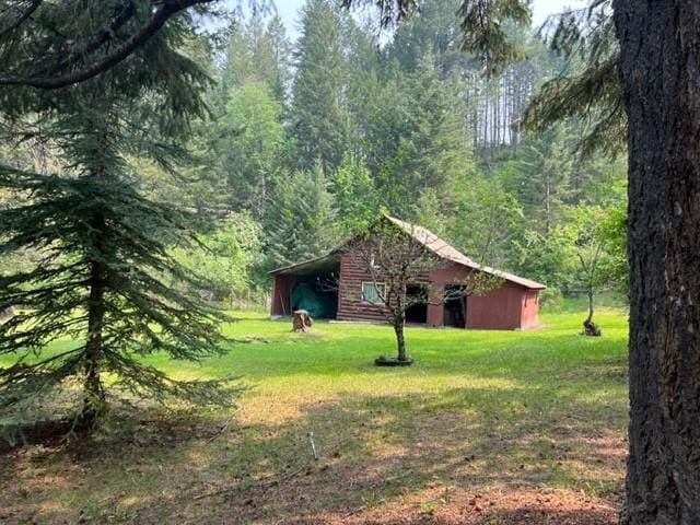 view of green lawn featuring a view of trees and an outbuilding