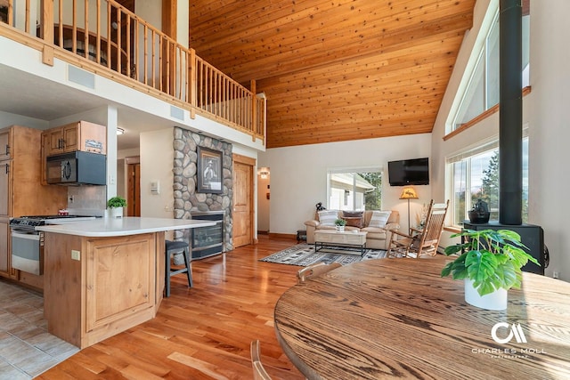 kitchen featuring high vaulted ceiling, stainless steel range with gas stovetop, black microwave, open floor plan, and a wood stove
