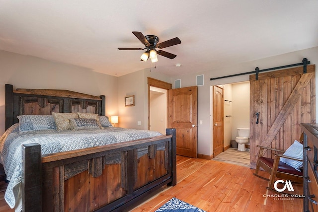 bedroom featuring light wood-style flooring, a barn door, connected bathroom, ceiling fan, and baseboards