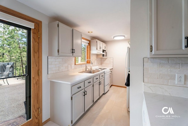 kitchen featuring white appliances, light countertops, decorative backsplash, under cabinet range hood, and a sink