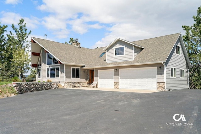 view of front facade with asphalt driveway, stone siding, a shingled roof, and a chimney