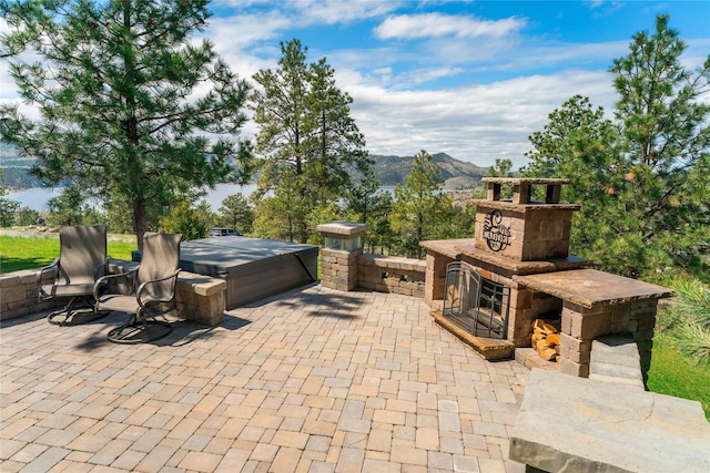 view of patio with an outdoor stone fireplace, a mountain view, and a hot tub