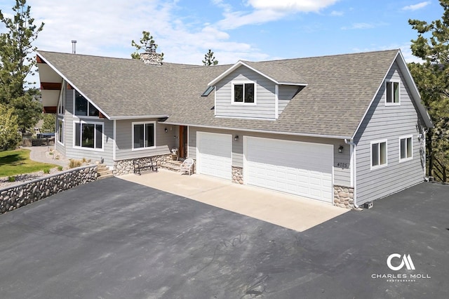 view of front of house featuring driveway, stone siding, a shingled roof, and a chimney