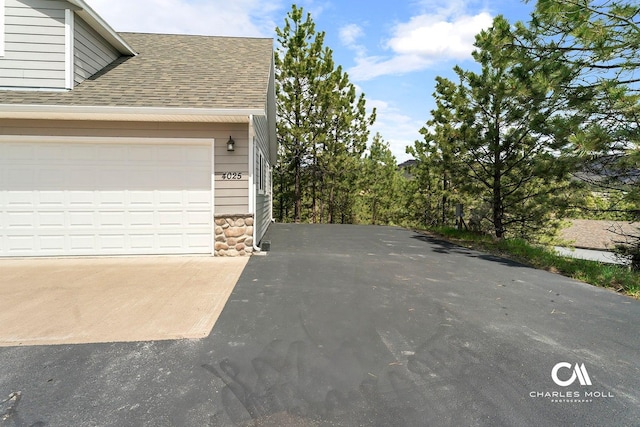 view of side of property featuring roof with shingles, driveway, and stone siding