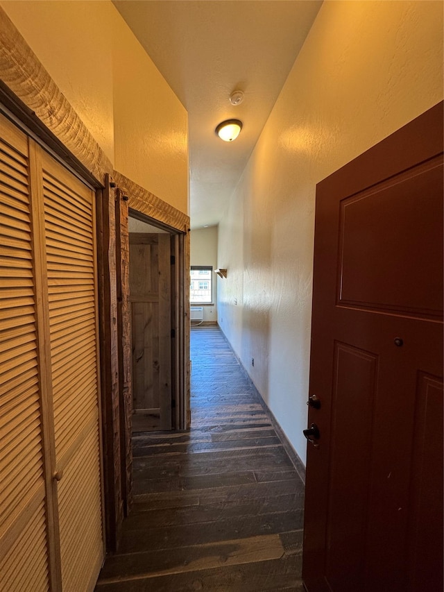 corridor featuring dark wood-style floors and a textured wall