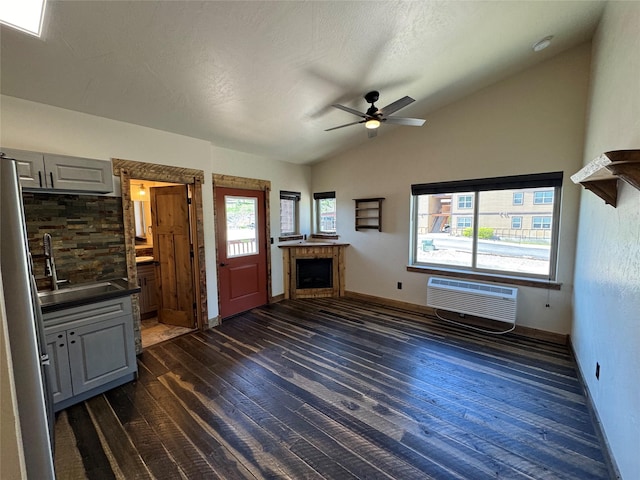 unfurnished living room with vaulted ceiling, a sink, dark wood-style flooring, a fireplace, and a ceiling fan