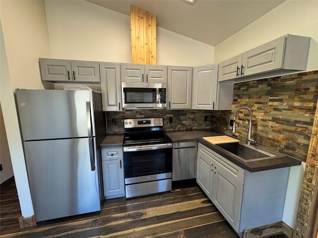 kitchen with stainless steel appliances, a sink, dark countertops, vaulted ceiling, and tasteful backsplash