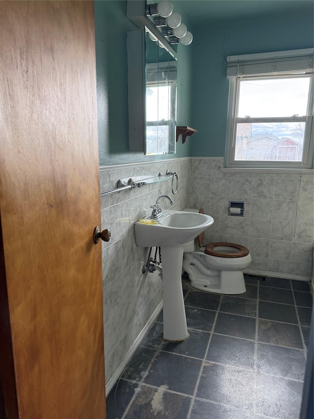 bathroom with tile walls, healthy amount of natural light, toilet, and a wainscoted wall