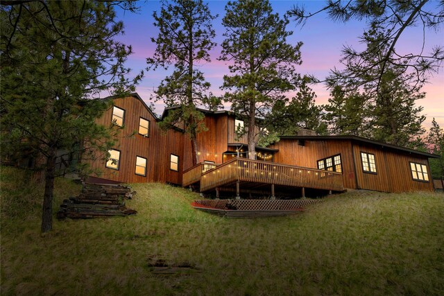 back of property at dusk with a wooden deck and a lawn