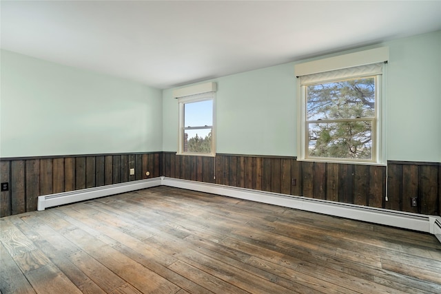 empty room with wainscoting, hardwood / wood-style floors, wooden walls, and a baseboard heating unit