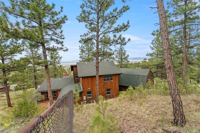 rear view of house featuring a shingled roof, fence, and an outdoor structure