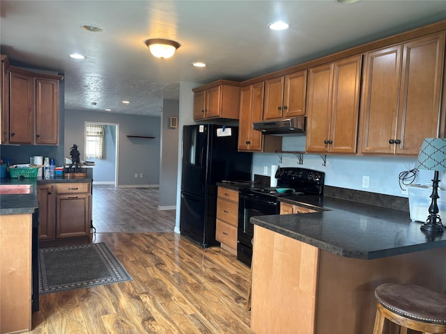 307 S Iowa St, Conrad, MT 59425 - kitchen with black appliances, under cabinet range hood, a peninsula, dark countertops, and wood finished floors