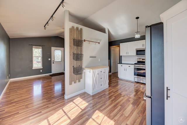 kitchen with appliances with stainless steel finishes, vaulted ceiling, track lighting, light wood-style flooring, and white cabinetry