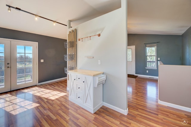 entryway featuring rail lighting, light wood finished floors, french doors, lofted ceiling, and baseboards