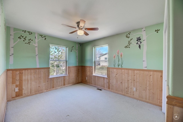 unfurnished room featuring a wainscoted wall, wood walls, ceiling fan, and carpet