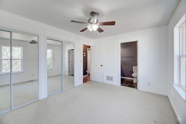 unfurnished bedroom featuring multiple closets, carpet, baseboards, connected bathroom, and a ceiling fan