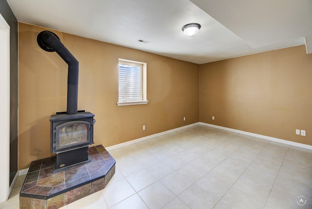 unfurnished living room featuring a wood stove, light tile patterned flooring, and baseboards