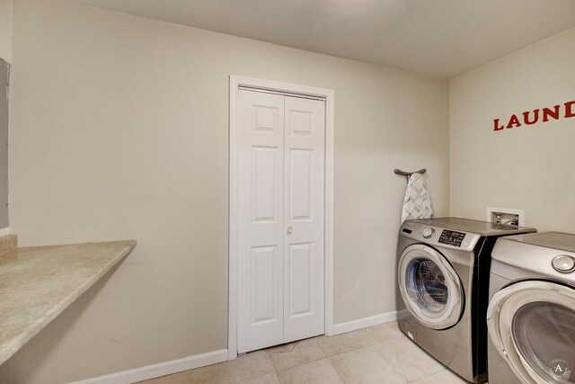 washroom with washing machine and dryer, baseboards, and light tile patterned floors