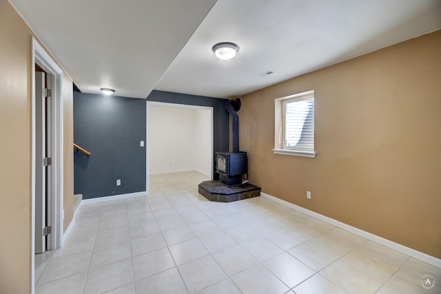 below grade area with a wood stove, stairs, baseboards, and light tile patterned floors