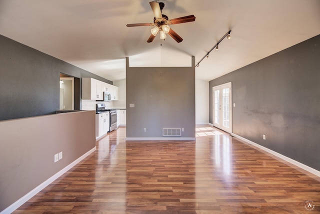 unfurnished living room featuring vaulted ceiling, ceiling fan, wood finished floors, rail lighting, and baseboards