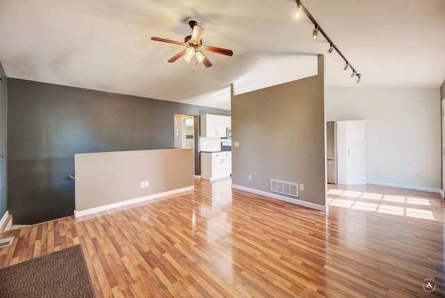 unfurnished living room with track lighting, a ceiling fan, light wood-type flooring, vaulted ceiling, and baseboards