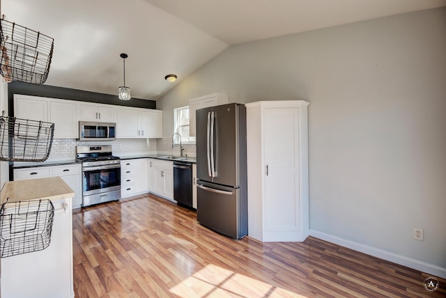 kitchen with stainless steel appliances, a sink, light wood-style flooring, lofted ceiling, and tasteful backsplash
