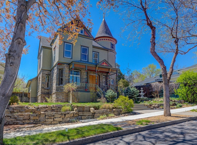 victorian home featuring stone siding, a porch, and fence