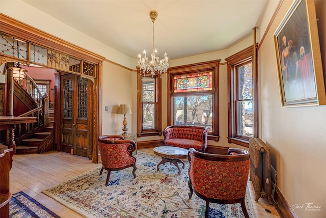 sitting room featuring a chandelier, hardwood / wood-style flooring, stairs, radiator heating unit, and baseboards