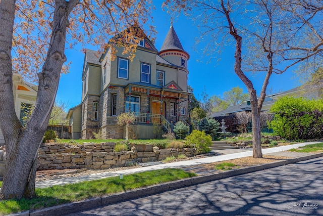 victorian-style house featuring stone siding, a porch, and fence