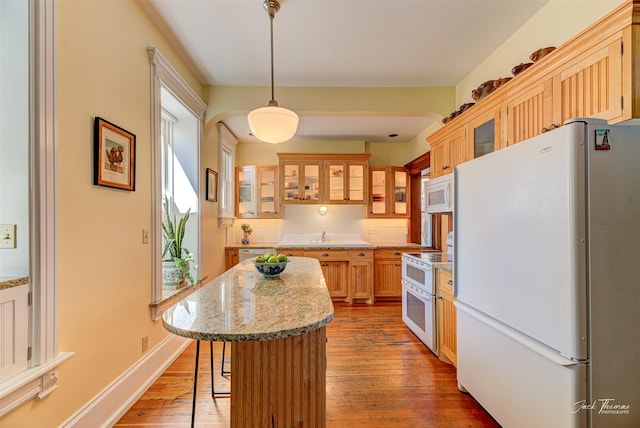 kitchen featuring white appliances, hardwood / wood-style flooring, a breakfast bar area, a kitchen island, and glass insert cabinets