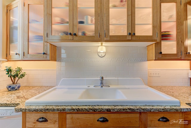 kitchen with decorative backsplash, a sink, glass insert cabinets, and white dishwasher
