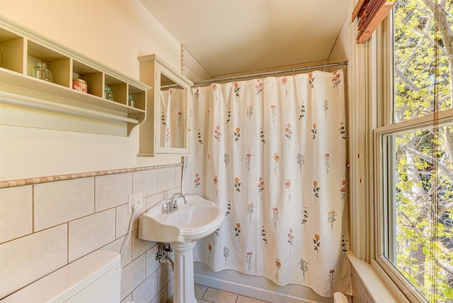 full bathroom with tile patterned floors, toilet, healthy amount of natural light, and tile walls