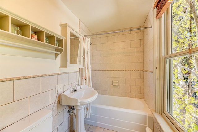 bathroom with tile patterned flooring, tile walls, shower / bathtub combination with curtain, toilet, and plenty of natural light