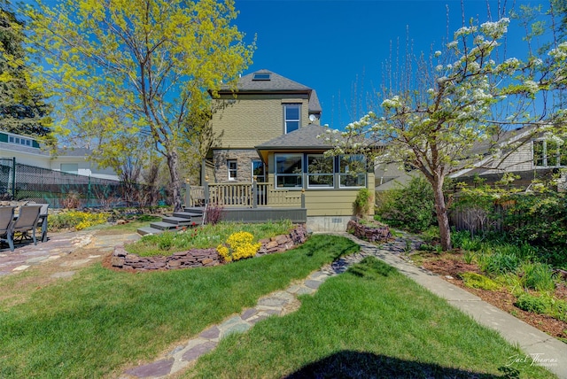 back of property with a deck, stone siding, and roof with shingles