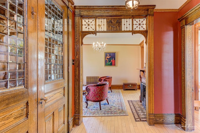 foyer with a chandelier, crown molding, light wood-type flooring, baseboards, and radiator heating unit
