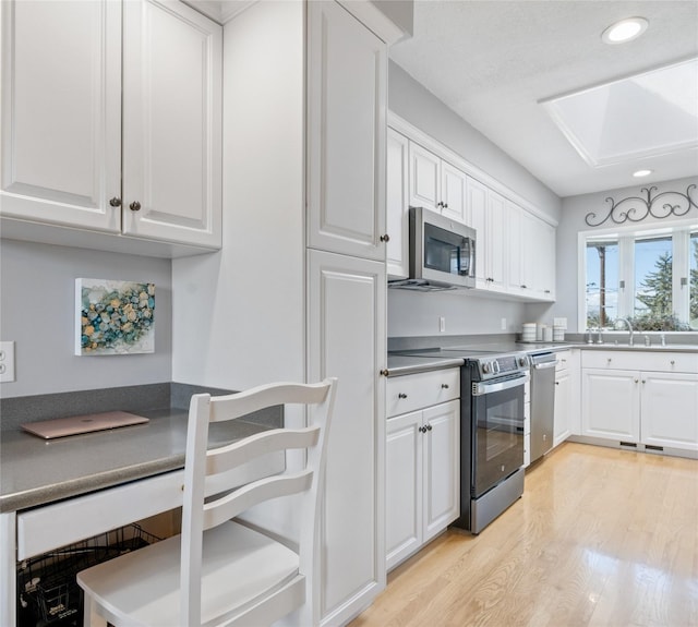 kitchen with stainless steel appliances, white cabinetry, light wood-style flooring, recessed lighting, and a skylight