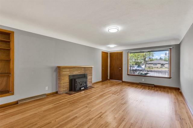 unfurnished living room featuring a wood stove, wood finished floors, baseboards, built in features, and a textured ceiling