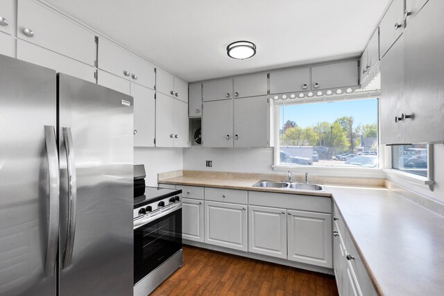 kitchen featuring appliances with stainless steel finishes, a sink, light countertops, and dark wood-style flooring