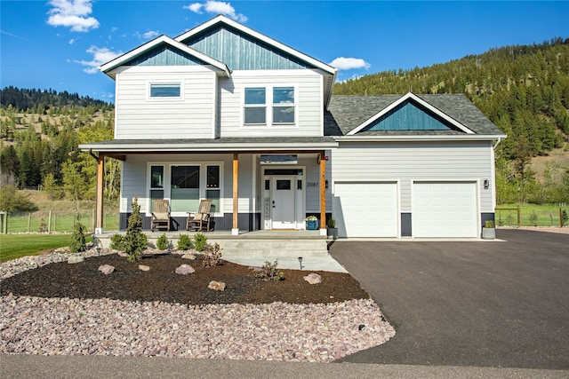 view of front of home featuring covered porch, roof with shingles, asphalt driveway, and a view of trees