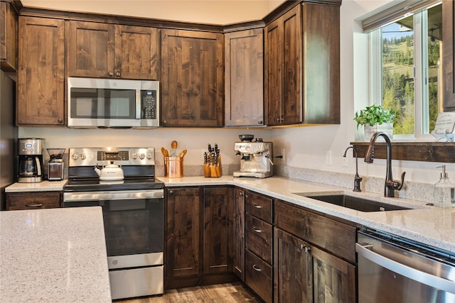 kitchen featuring stainless steel appliances, a sink, light stone counters, and dark brown cabinets