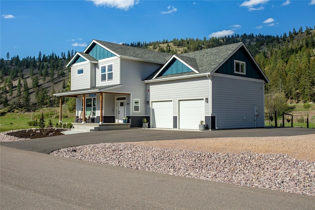 view of front facade featuring a porch, board and batten siding, asphalt driveway, a garage, and a forest view