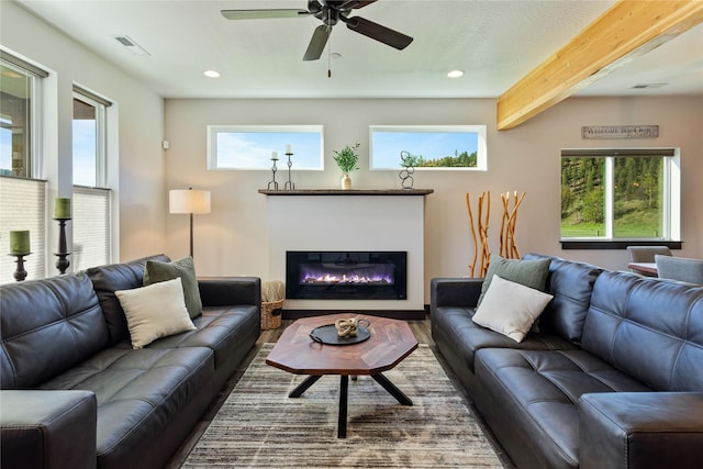 living area featuring a glass covered fireplace, beamed ceiling, ceiling fan, recessed lighting, and wood finished floors