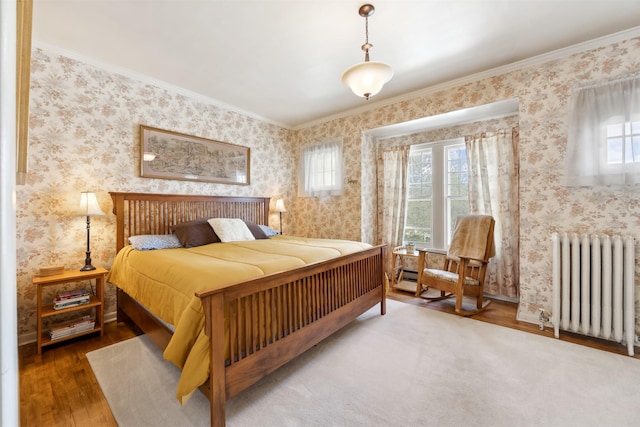 bedroom featuring radiator heating unit, wood finished floors, multiple windows, ornamental molding, and wallpapered walls