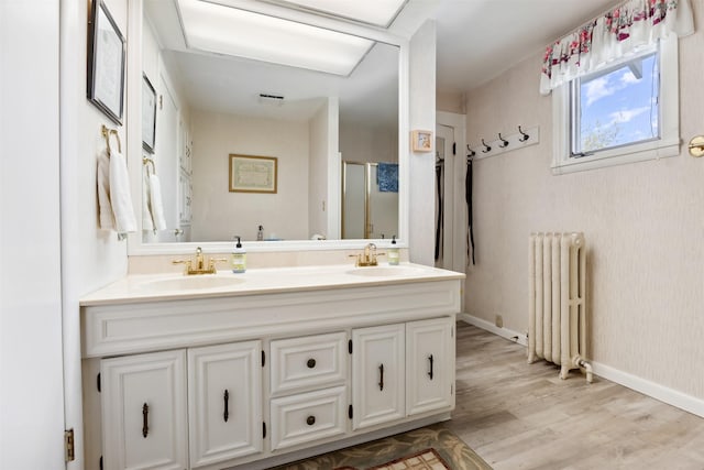 bathroom featuring radiator heating unit, double vanity, a stall shower, and wood finished floors